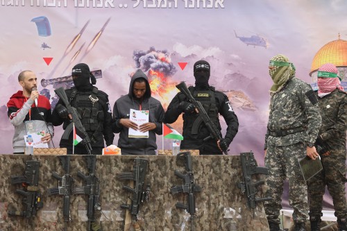 Israeli hostages Averu Mengistu (4th-R) and Tal Shoham (L) are flanked by Hamas fighters as they stand on a stage during their release in Rafah in the southern Gaza Strip on February 22, 2025. Masked militants paraded Tal Shoham and Averu Mengistu on stage in the southern Gazan city of Rafah before handing them over to officials from the Red Cross. (Photo by Omar AL-QATTAA / AFP) (Photo by OMAR AL-QATTAA/AFP via Getty Images)